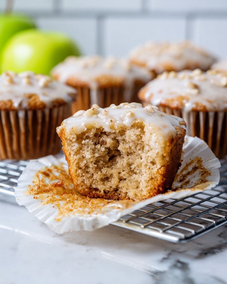 The image shows a close-up of nine muffins in a silver muffin pan, each topped with a shiny, light beige glaze that covers the bumpy, rough-textured muffin surface. The muffins are golden brown with small, uneven lumps poking out under the glaze, giving them a rustic look. The metal pan has soft scratches and minor stains, and a shadow falls diagonally across the top left and bottom right corners, adding depth to the scene. The background is a white marbled texture. Photo taken with an iphone --ar 4:5 --v 7