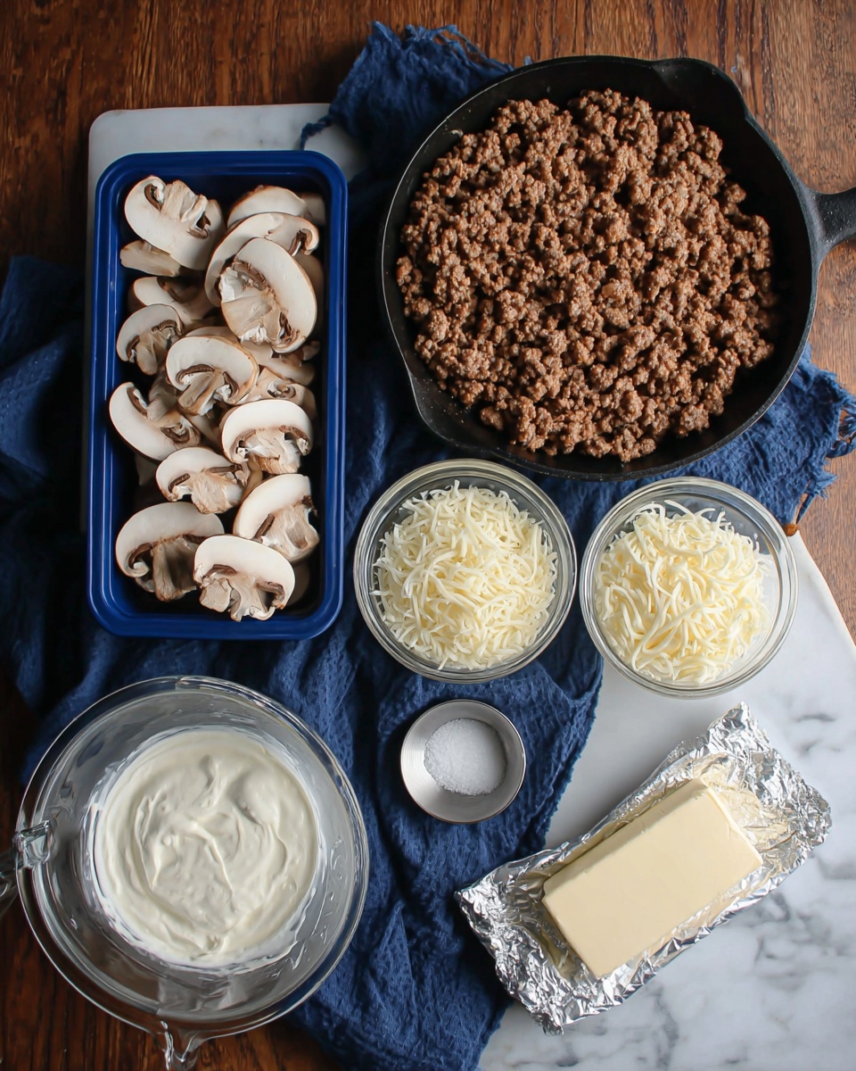 The image shows a black skillet filled with cooked ground meat, placed on a white marbled surface with a dark blue cloth beneath it. Next to the skillet, there are two blue plastic containers filled with sliced brown mushrooms, positioned one above the other. In front of the skillet, a clear glass bowl holds shredded white cheese, beside a transparent measuring cup filled with smooth white cream cheese. A small metal cup containing salt is placed near the cheese items. At the bottom right, there is a silver wrapped block of butter on the white marbled surface. photo taken with an iphone --ar 4:5 --v 7
